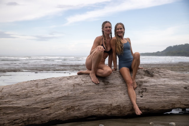 Instructors: Schuyler Grand and Nikki Vilella sitting on a large driftwood tree on the beach in Costa Rica